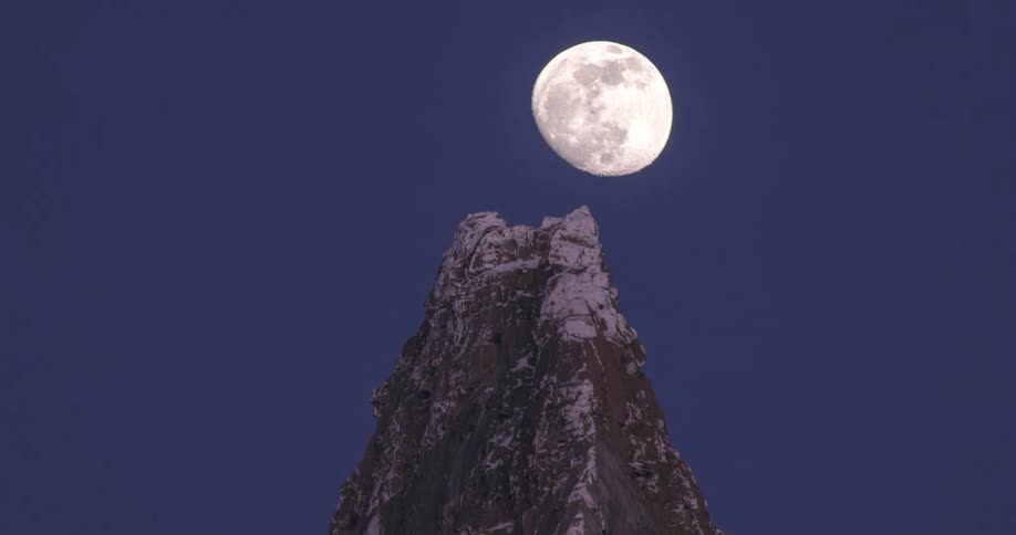 A glowing moon rises behind a mountain peak in the deep blue sky