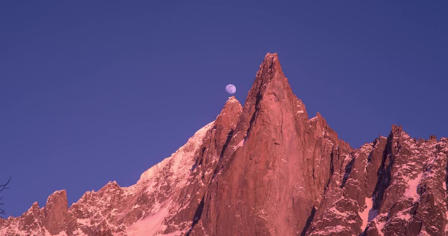 A time lapse of a mountain peak shows the moon rising overhead