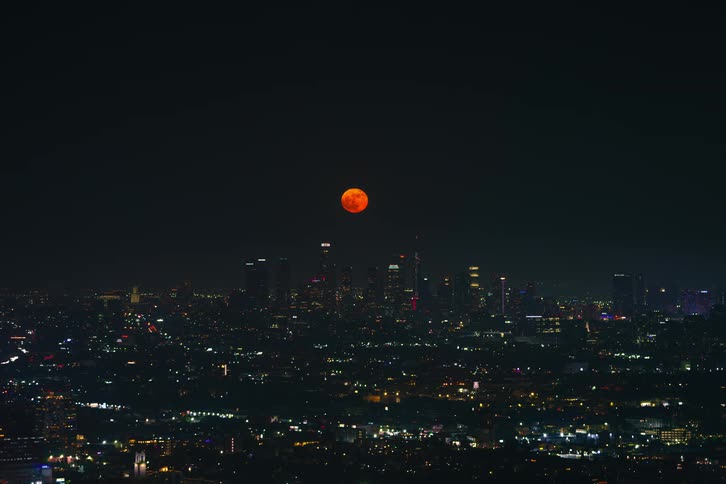 Time lapse of a red moon rising over the skyline of the city at nighttion