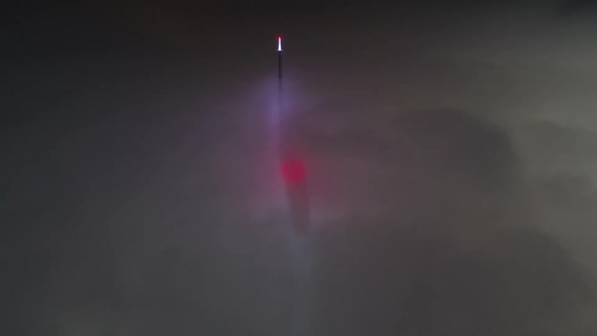 A light beacon flashing in the distance on a black pole as dense fog rolls in front of it
