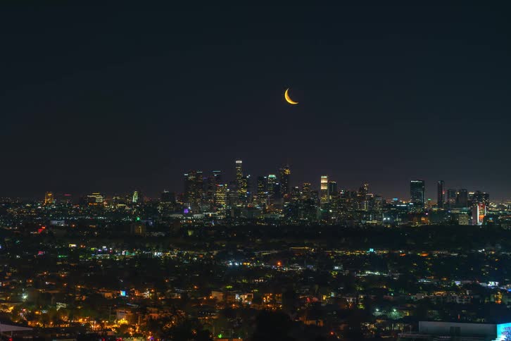 A night view of a city skyline as the moon rises above the skyscrapers