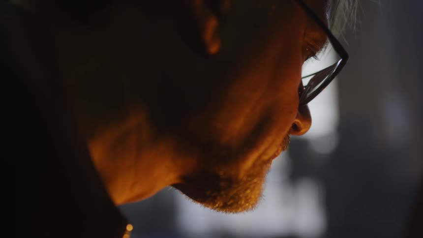 A man wearing glasses has his face illuminated by a light source in front of him