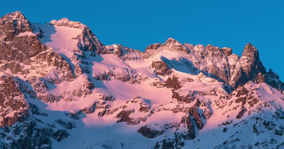 Time lapse of a mountain peak covered in snow changing colors during sunrise
