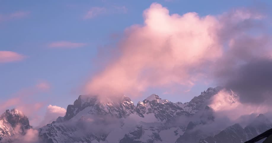 A time lapse of a snow covered mountain has clouds billowing around it