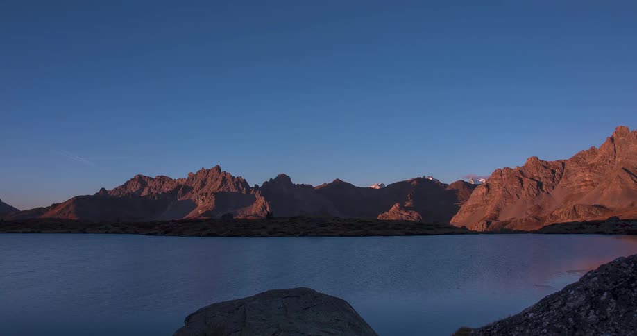 Ripples flow across reflective surface of water near mountains under a clear sky
