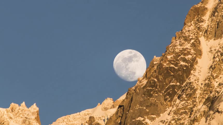 A full moon above a sloped rocky mountainside in the daytime