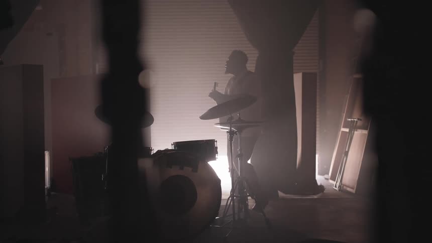 A man standing next to a drum set while playing guitar in a garage