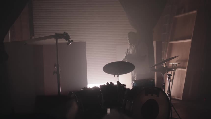 A man standing next to a drum set while he plays guitar in a garage