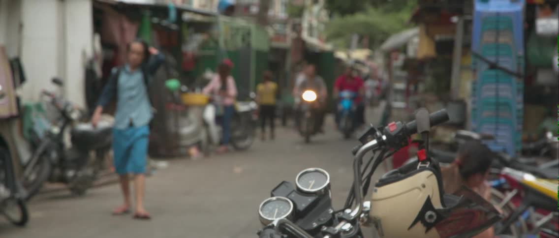 People walk and ride scooters down a busy street