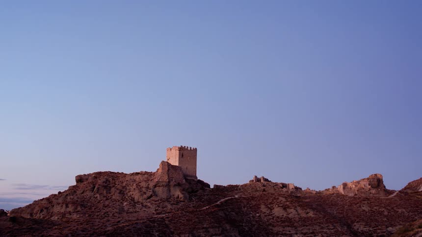 The sun sets and stars come out over an old fort on a hill