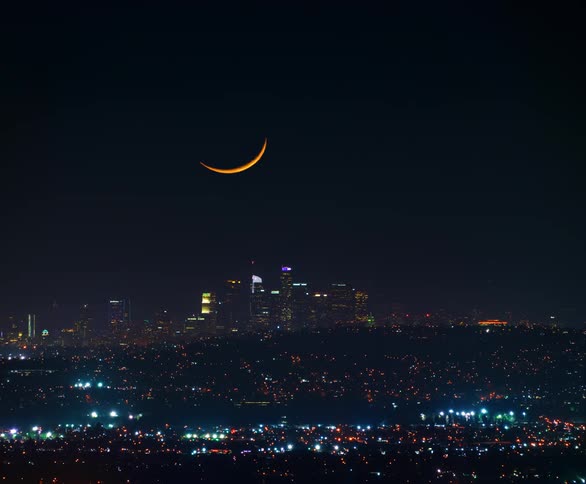 The skyline of a city at night with the moon travelling below the horizon