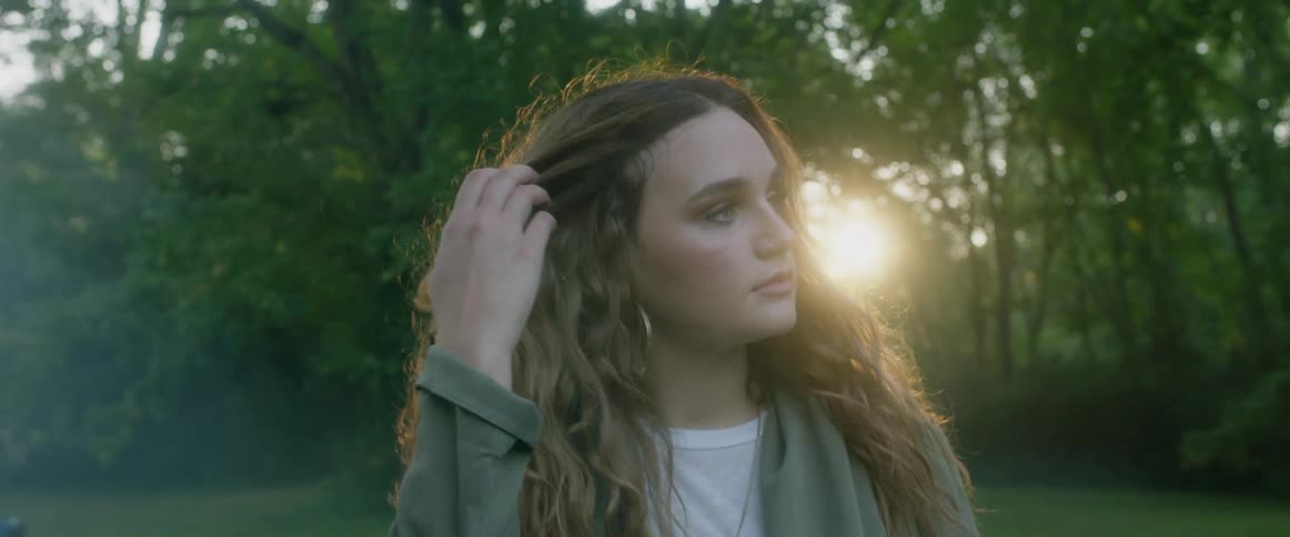 A young woman with curly hair brushes her hair over her ear in the sunset