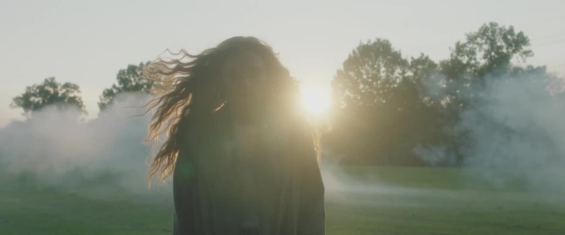 A woman walks along a field with fog behind her