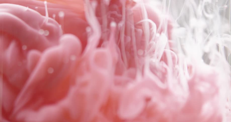 A pinkish red substance pours into a clear liquid