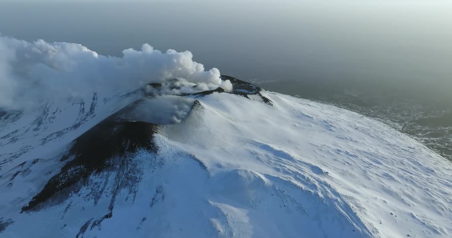 Clouds obscure the top of a snowy mountain ridge during the day