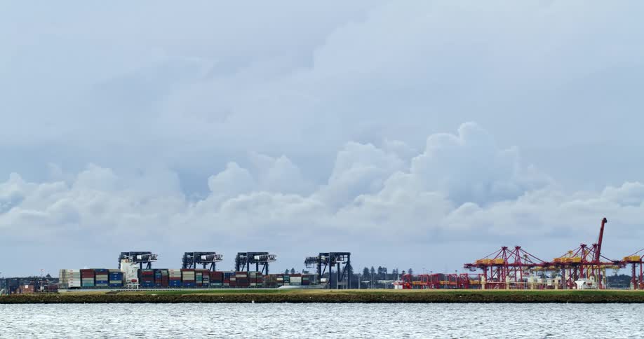 A wide shot of a shipping dock with shipping containers lined up and cranes to move them
