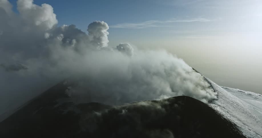 An aerial of a tall mountain with fog rolling across the mountain