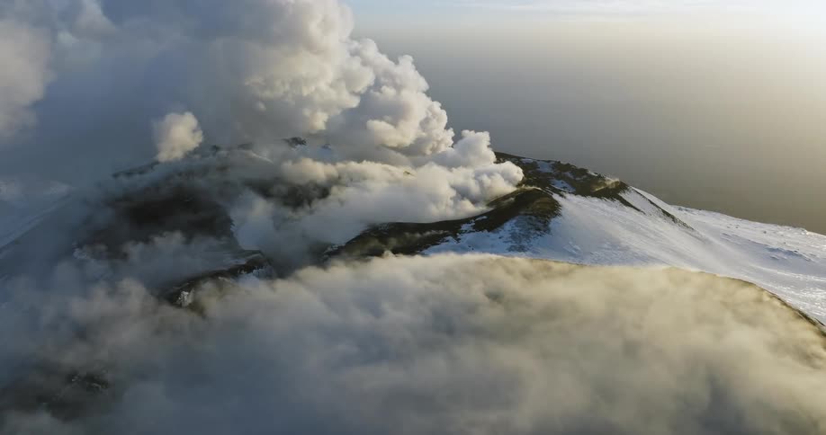 White smoke rises from snow covered volcanos on a sunny day