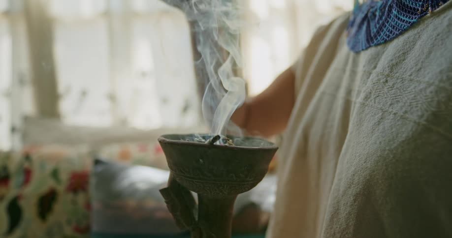 A woman waving her hand over a bowl of burning incense