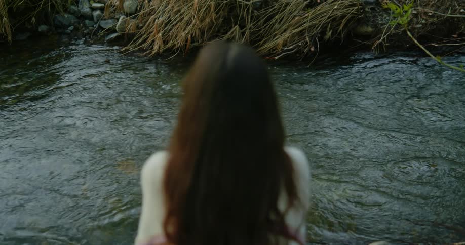 A woman sits along a river bank