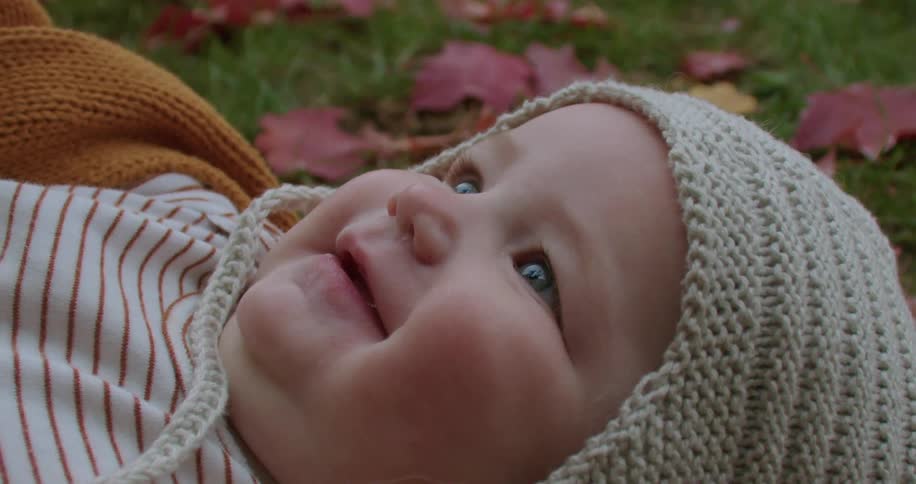 A close up of a babies face while laying on the grass smiling