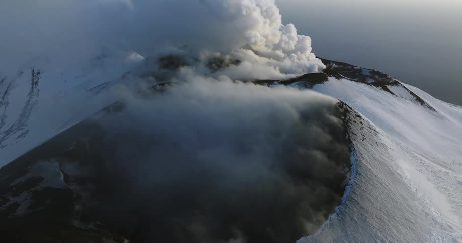 Billowy smoke is coming out of a volcano that is covered in and surrounded by snow and ice