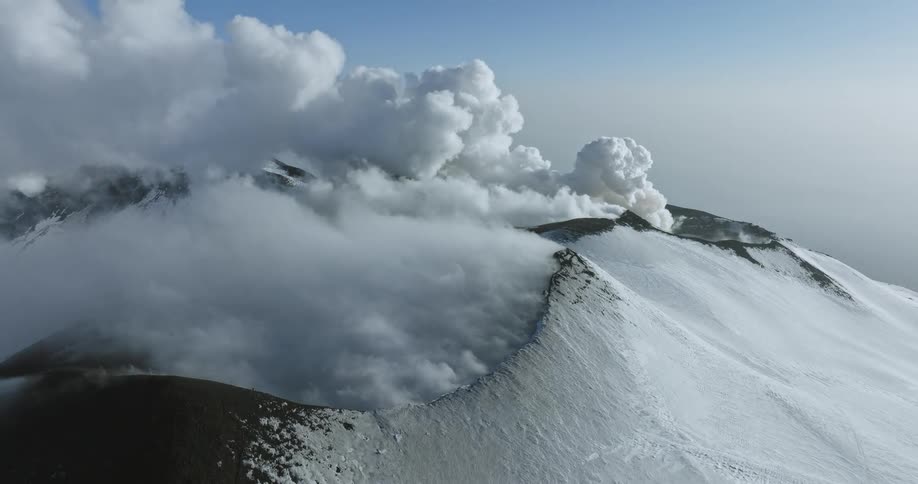 An enormous volcano with snow on it releases a huge cloud of steam