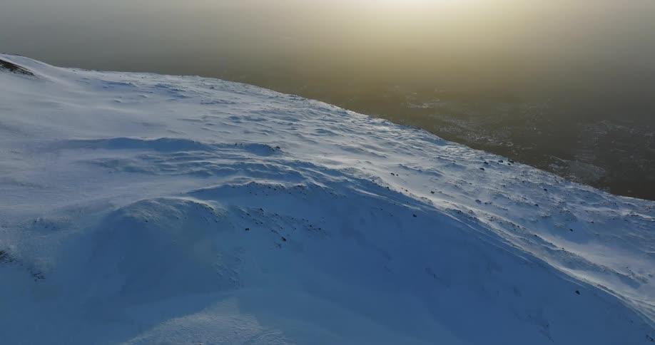 An aerial of a snow covered mountain with a wide open ocean beyond