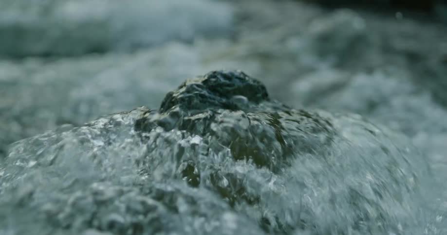 Water rapidly flows in a stream and splashes as it moves over a rock