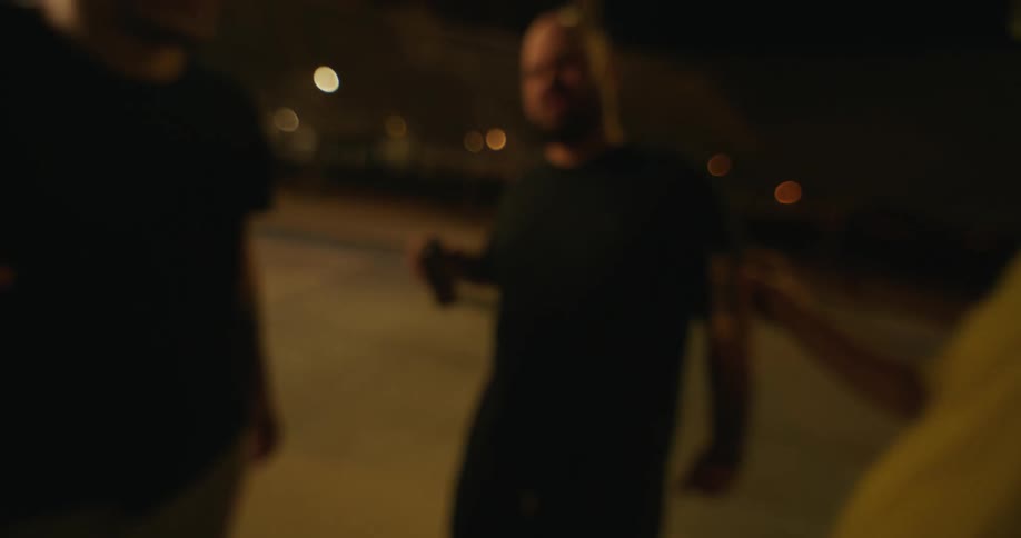 Three men standing outside at nighttime in a parking lot toasting with three beer cans or energy drinks