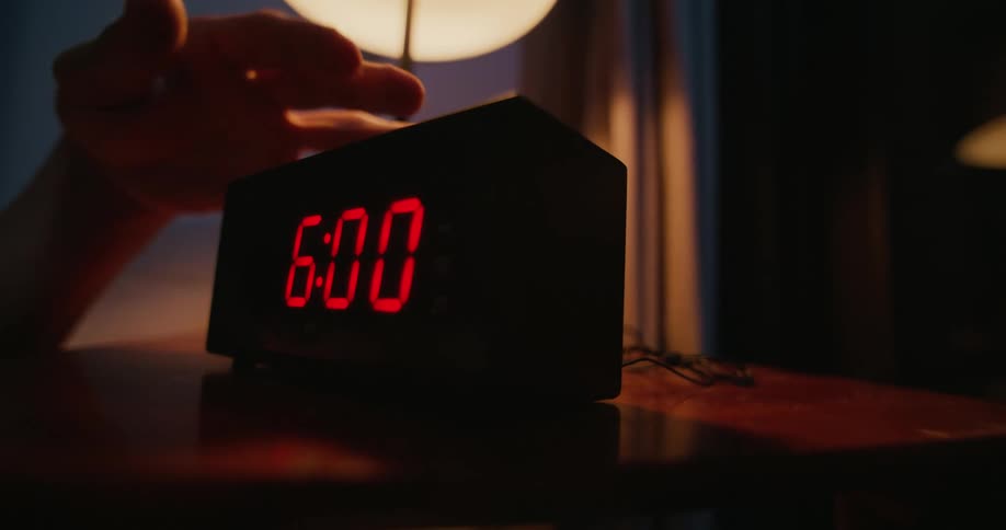 A person is setting their alarm clock in the morning