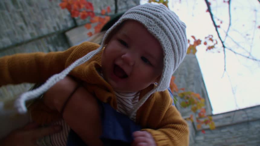 Mother playfully holds and swings her baby in front of the camera outside at daytime