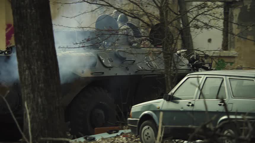 Two soldiers aiming weapons ride armored vehicle past graffiti covered buildings