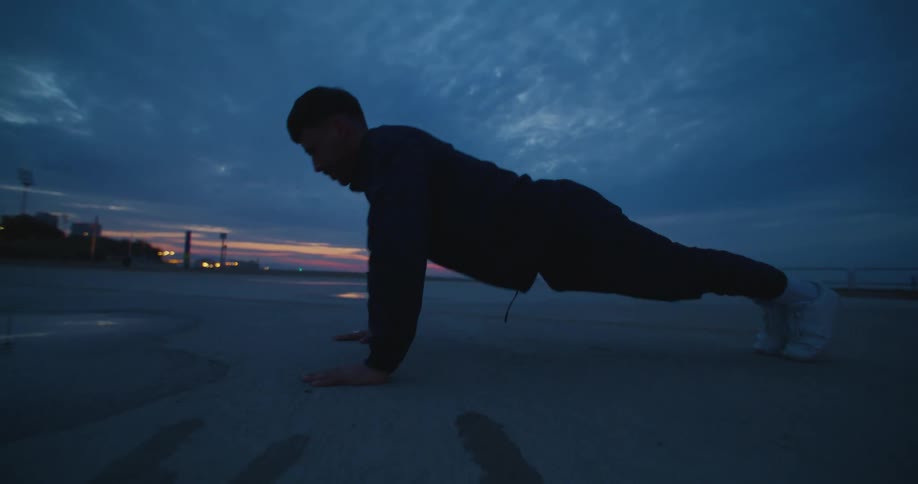 A man doing push ups outside on concrete at dusk
