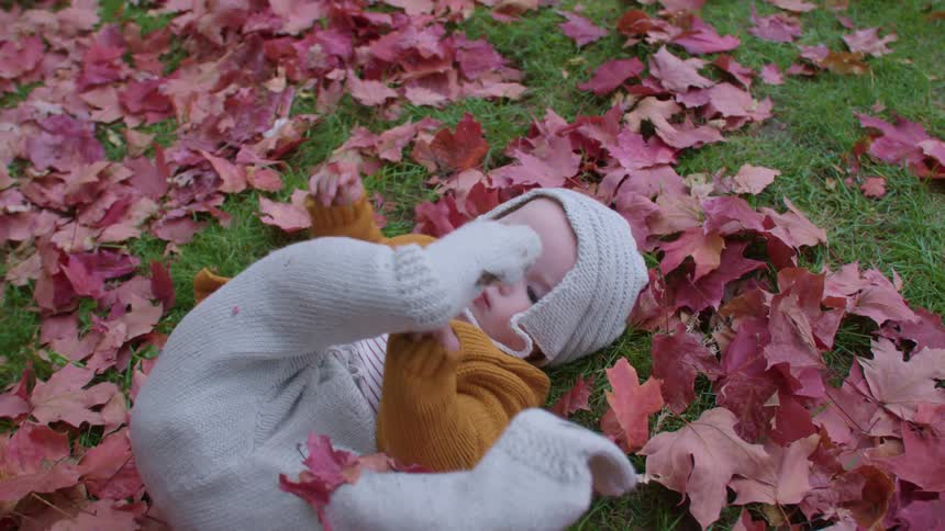 A baby rolls around in leaves outdoors