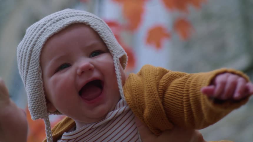 Blonde mother with green hat holds up baby laughing