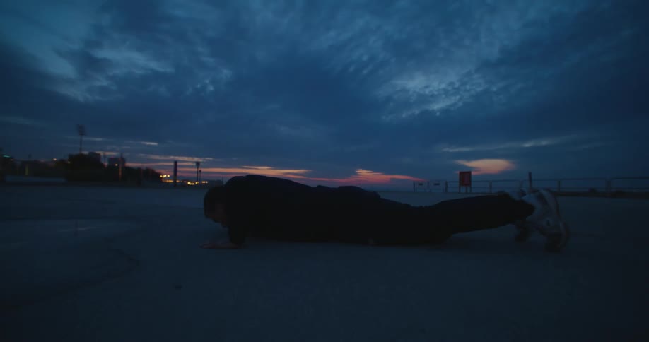 A man is doing pushups outdoors while the sun is setting