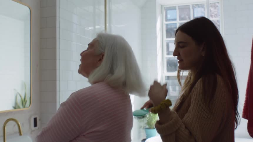 Young woman in bathroom with grandma talking and brushing grandmas hair