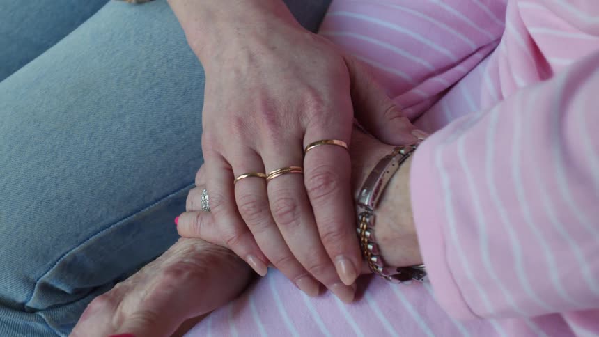 A young woman is holding the hand of an elderly woman