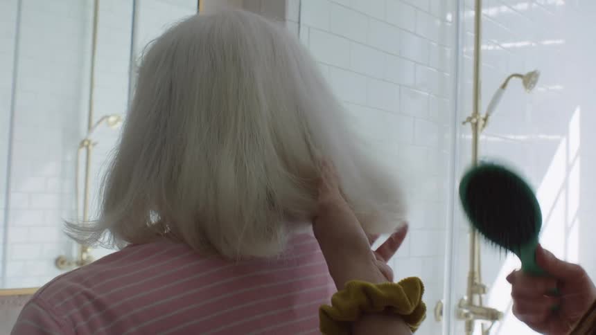 Woman combs the long white hair of an elderly woman in the bathroom