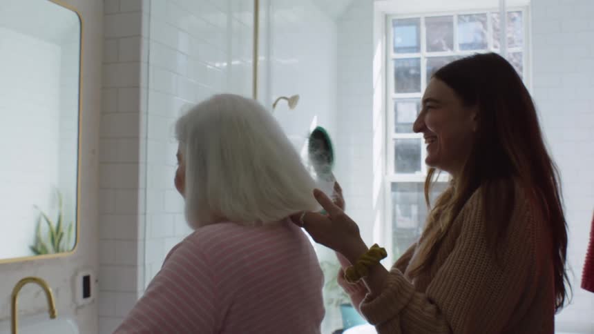 Young woman with grandma in the bathroom laughing and brushing her hair