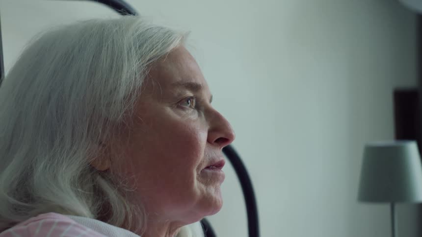 Woman touches back of hand to forehead of elderly woman lying in bed to check her temperature