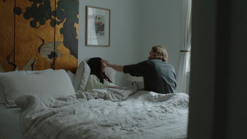 A woman comforts his partner while she lies in bed