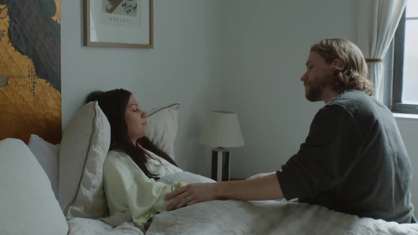 A man kisses his partner on the head while she lies in bed