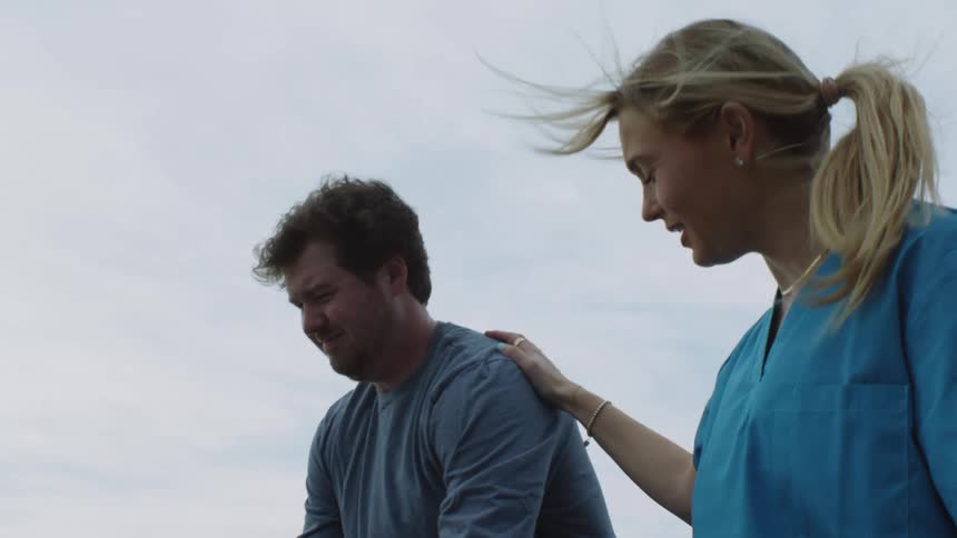 A young nurse encourages a man to learn to walk again using physical therapy parallel bars outdoors
