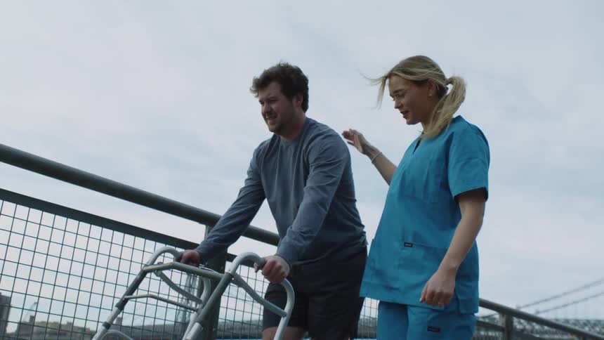 A nurse walks next to a man with his foot in a brace as he uses a walker