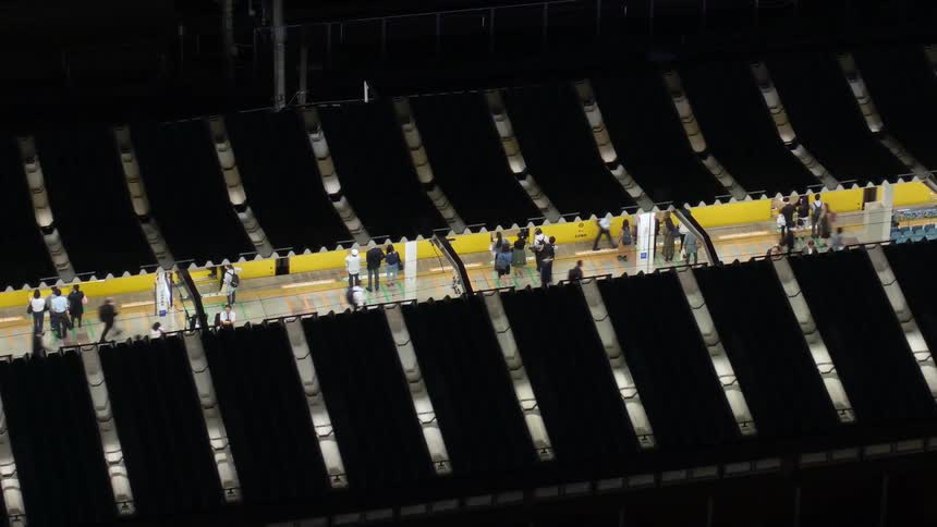 Time lapse aerial view of crowds of people boarding trains on a station at night