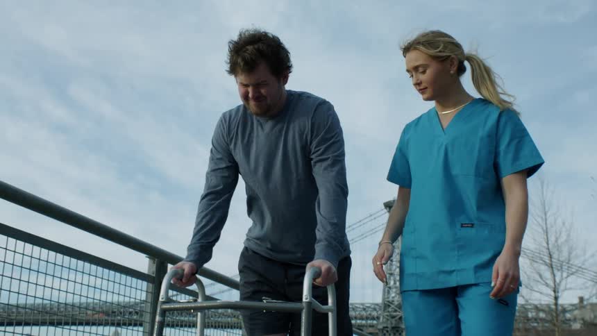 Therapist helps man using a walker in a park near to recover from an injury