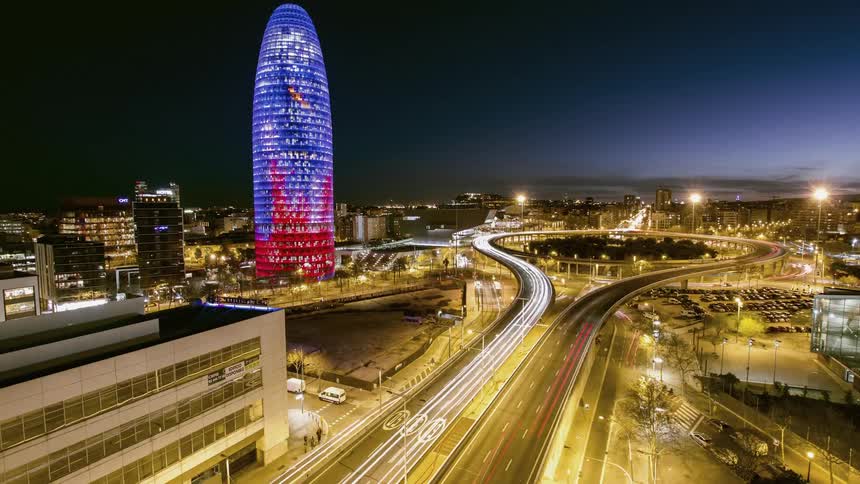 A time lapse of a city highway and a tall building lit up with blue lights showing dusk till night