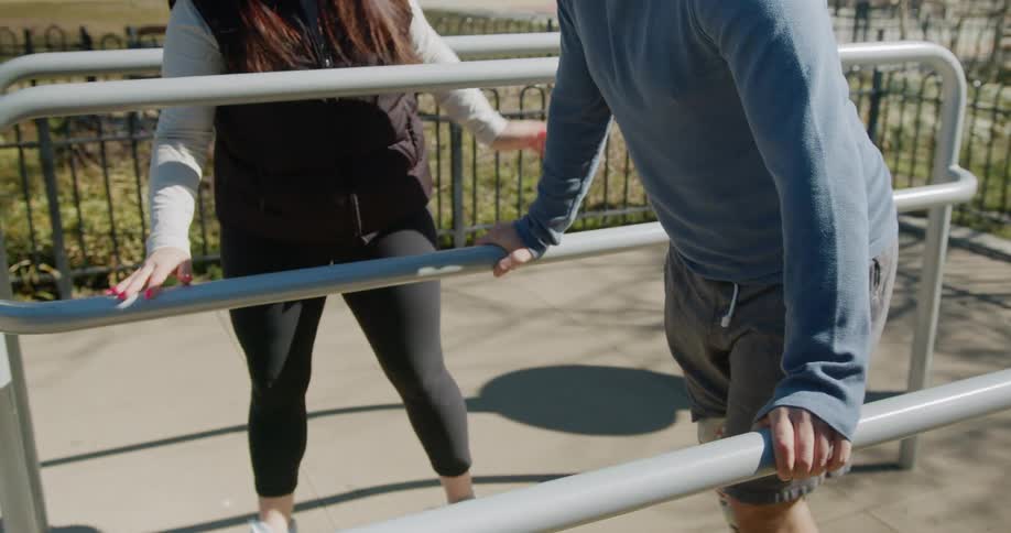 A young woman helps a man with an artificial leg learn to walk using parallel bars outdoors